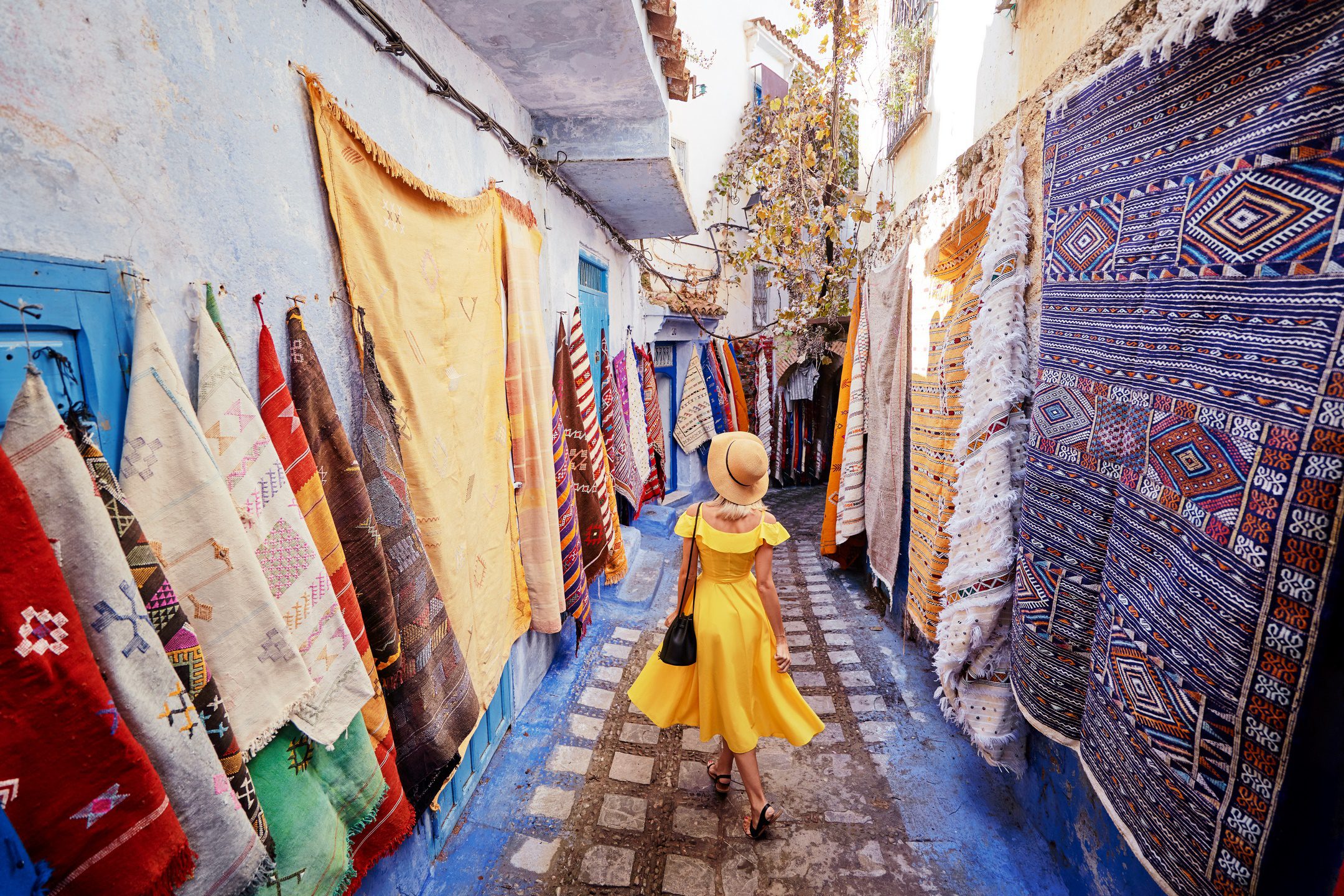 Colorful traveling by Morocco. Young woman in yellow dress walking in medina of blue city Chefchaouen.