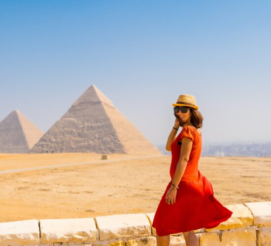 A tourist girl in a red dress at the Pyramids of Giza, the oldest Funerary monument in the world. In the city of Cairo, Egypt