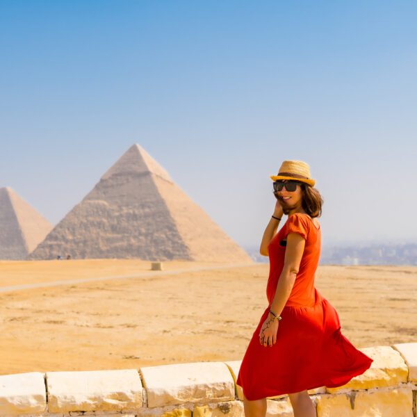 A tourist girl in a red dress at the Pyramids of Giza, the oldest Funerary monument in the world. In the city of Cairo, Egypt