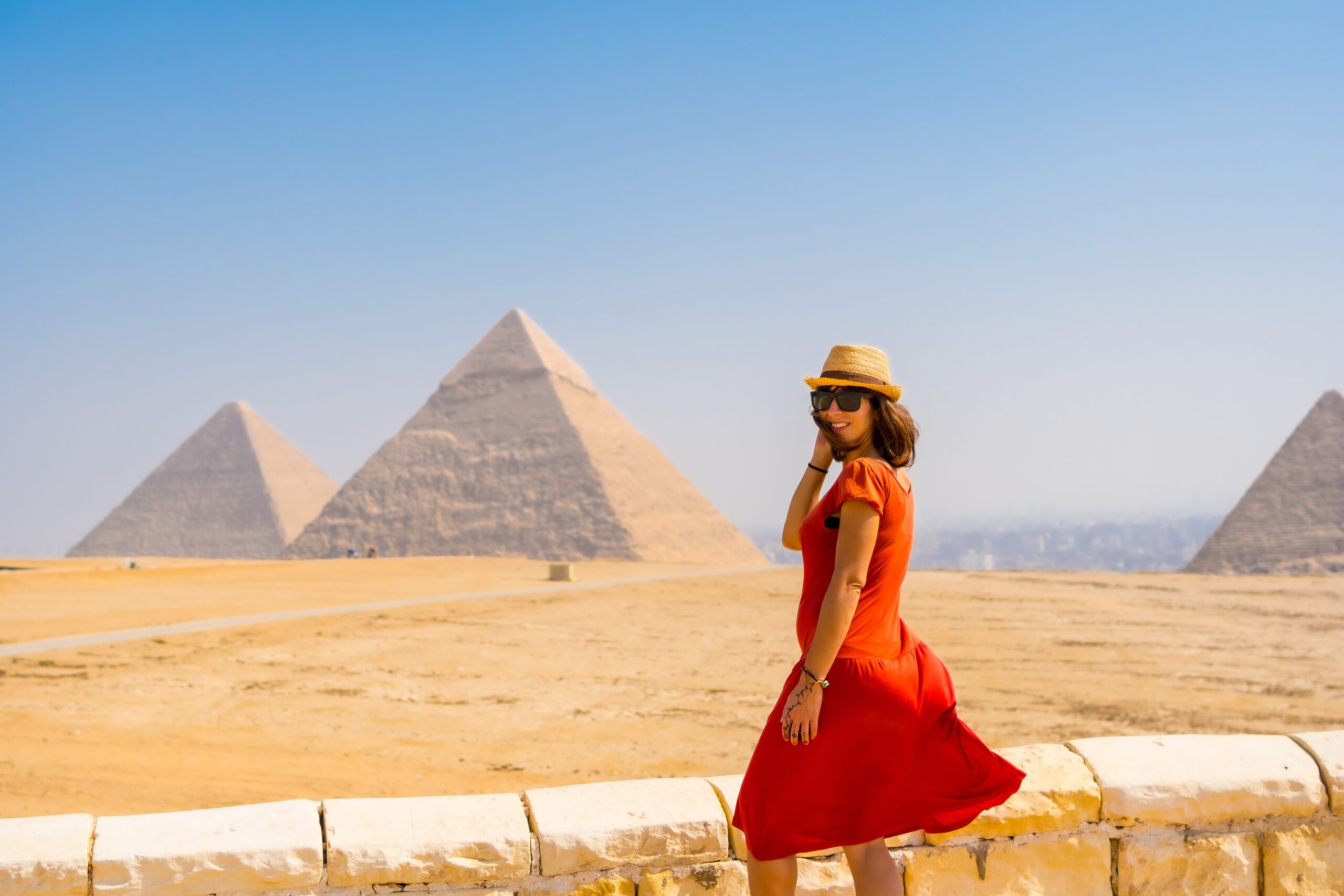 A tourist girl in a red dress at the Pyramids of Giza, the oldest Funerary monument in the world. In the city of Cairo, Egypt