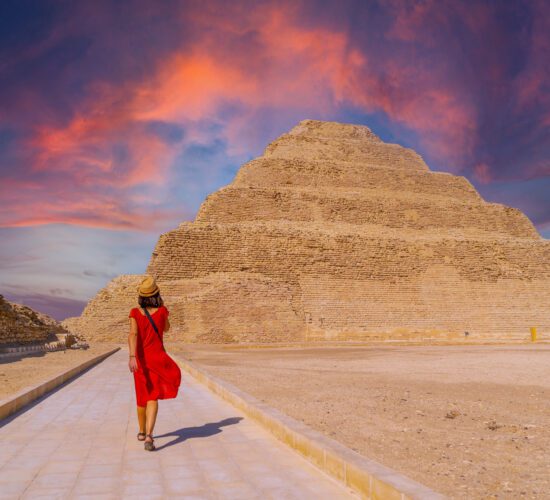 A young tourist in a red dress at the Stepped Pyramid of Djoser at sunset, Saqqara. Egypt. The most important necropolis in Memphis. The first pyramid in the world