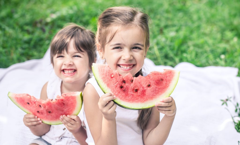 Balkan Tours: two little cute baby girls sisters eating watermelon in nature, playing and having fun, baby food concept and family time spending